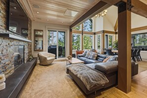 A spacious living area with a fireplace, leather sofas, and large windows offering a view of the outdoors.