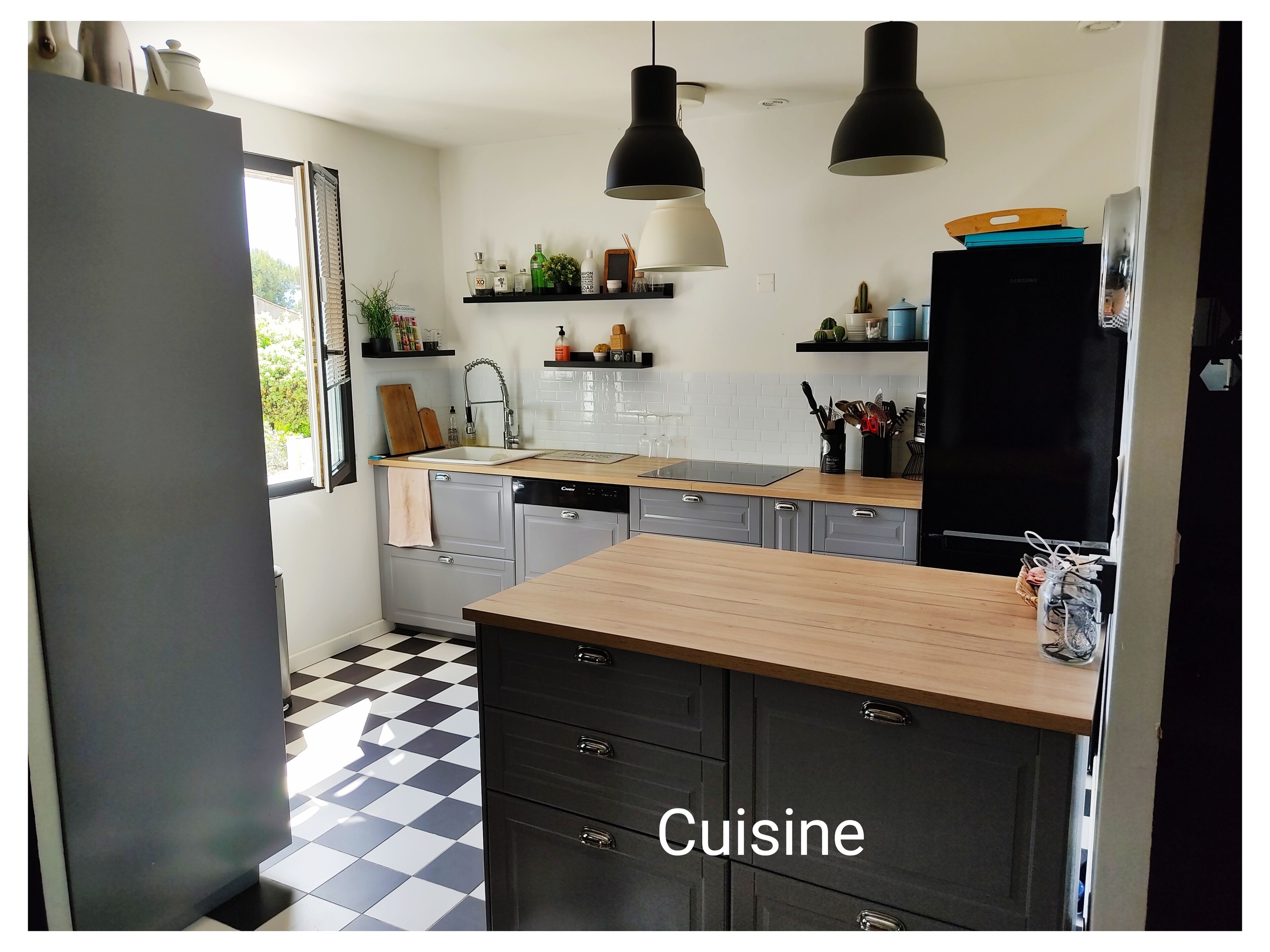 A modern kitchen with a black and white checkered floor, grey cabinetry, and a wooden island.