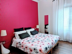 Une chambre à coucher avec un grand lit, un mur rouge à texture, un miroir et une fenêtre avec des rideaux.