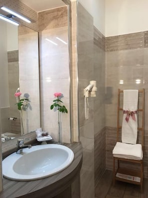 Une salle de bain avec un lavabo blanc, un miroir, un porte-serviettes et un espace douche.
