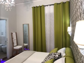 Une chambre d’hôtel avec un lit, une chaise, un miroir et une salle de bain visible à travers une porte ouverte.