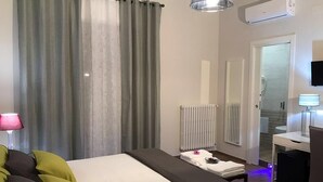 Een hotelkamer met een bed, bureau, spiegel, radiator en douchehoek.