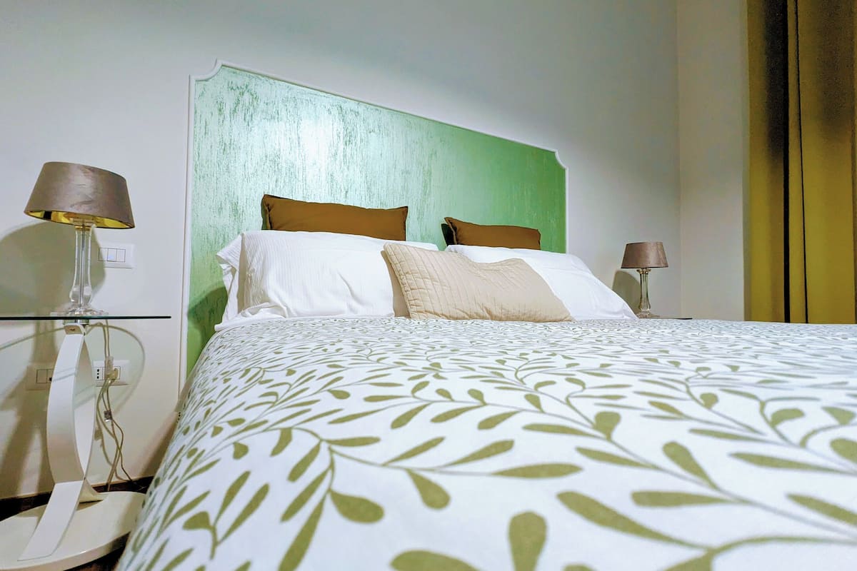 Un lit bien fait, avec une couvre-lit à motifs de feuilles, deux oreillers et une tête de lit verte.