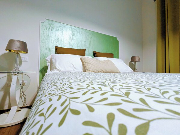Una cama bien hecha con una colcha de estampado de hojas, dos almohadas y un cabecero verde.