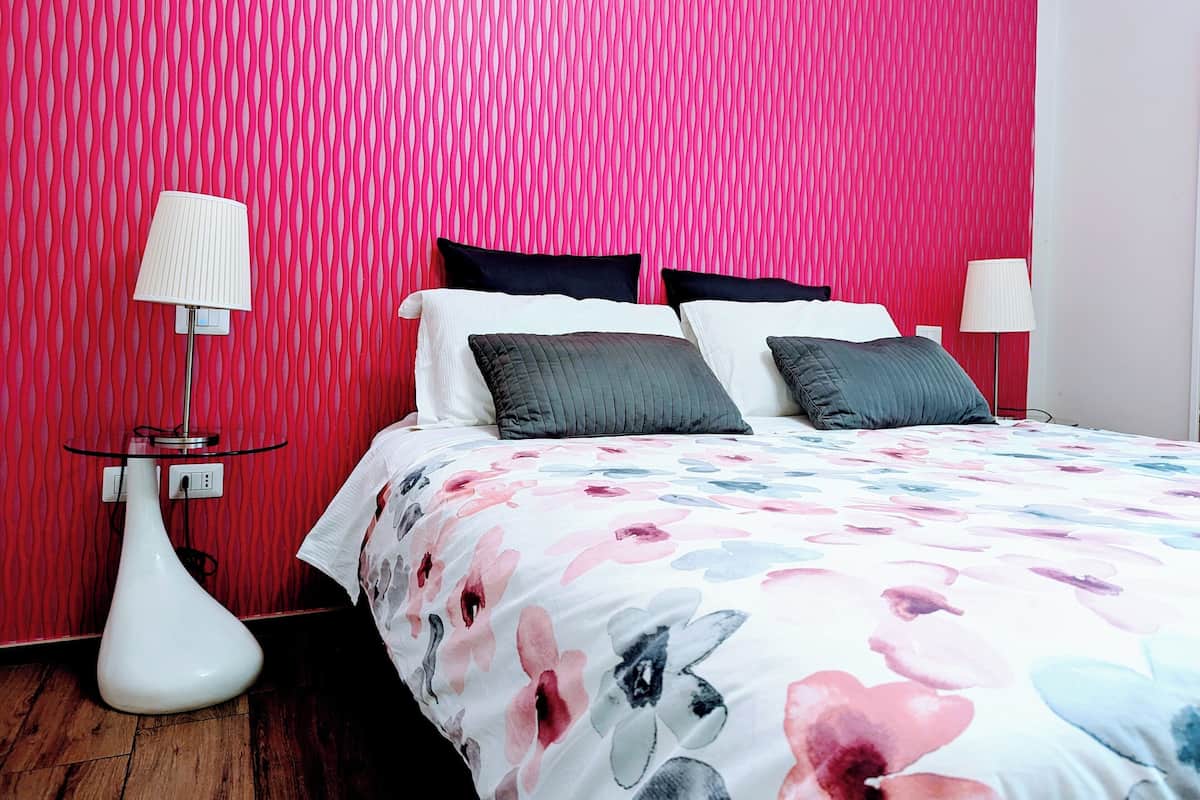 Une chambre à coucher moderne avec un mur rose vif, une couvre-lit à motifs floraux et deux lampes de chevet.