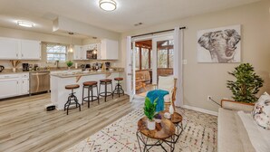 A modern kitchen with white cabinets, a wooden island with stools, and a dining area with a round table and chairs. - Downstairs BR! Pet Friendly house w/4BR, fenced yard & Sun Room (Indianapolis)