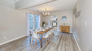 A dining area with a long wooden table, white chairs, and a chandelier. - Downstairs BR! Pet Friendly house w/4BR, fenced yard & Sun Room (Indianapolis)