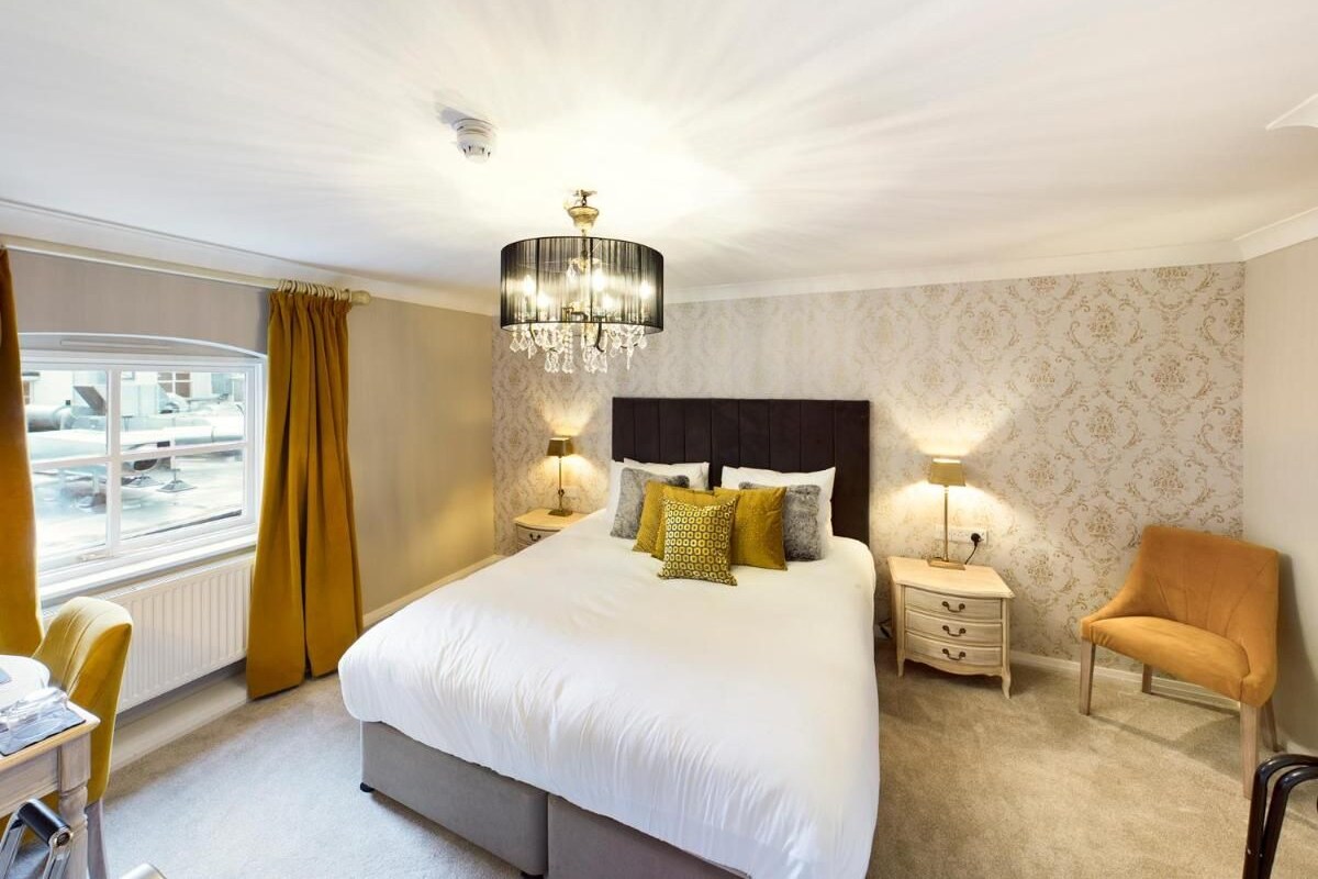 A bedroom with a large bed, two bedside tables with lamps, a chair, and a view of an airport through a window.