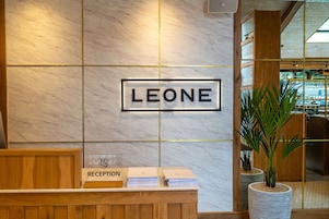 Uma mesa de recepção com uma placa que diz 'LEONE' e uma placa indicando a área de recepção.