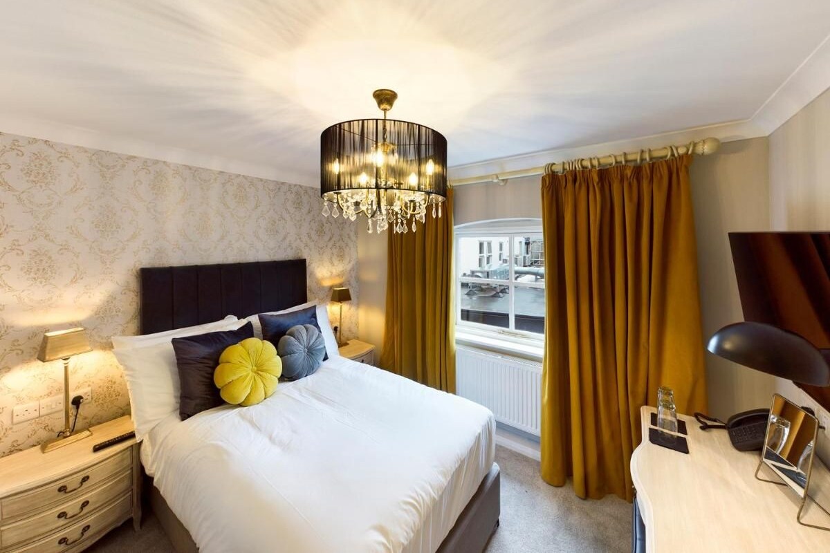 A well-lit bedroom with a large bed, a bedside table with a lamp, and a view of the city through a window.
