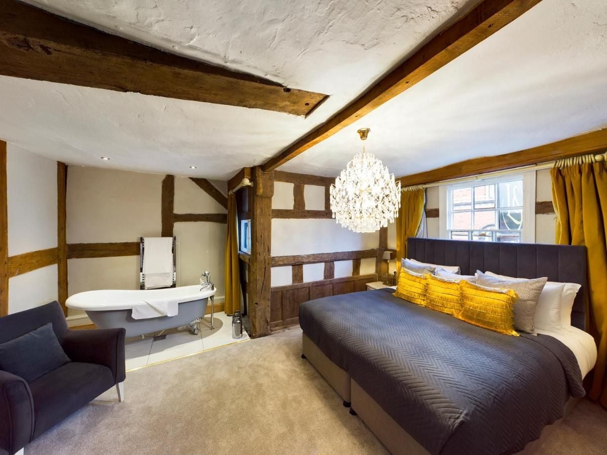 A bedroom with a large bed, a sitting area with a sofa, a bathtub, and a chandelier.