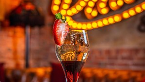 A cocktail glass with a strawberry garnish on a wooden table, with a neon sign in the background. - Lion & Swan Hotel (Congleton)