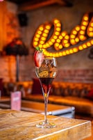 Um copo de cocktail com morango numa mesa de madeira, com um letreiro de néon ao fundo.