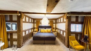 A bedroom with a large bed, a chandelier, wooden beams, and a yellow chair. - Lion & Swan Hotel (Congleton)