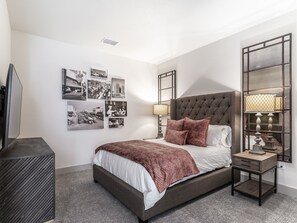 Un dormitorio ordenado con una cama grande, mesitas de noche, un televisor y una pared decorada con fotografías en blanco y negro.