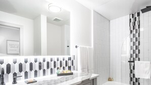 A modern bathroom with a marble vanity, a large mirror, a shower with a black and white tile pattern, and a white bathtub.