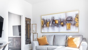 A modern living room with a grey sectional sofa, a flat-screen TV, and a large abstract painting on the wall.