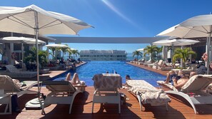 Ein Poolbereich mit Liegestühlen und Sonnenschirmen, freie Sicht auf den Pool sowie ein Gebäude im Hintergrund.