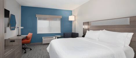 A hotel room with a bed, a desk, a chair, a lamp, and a window.
