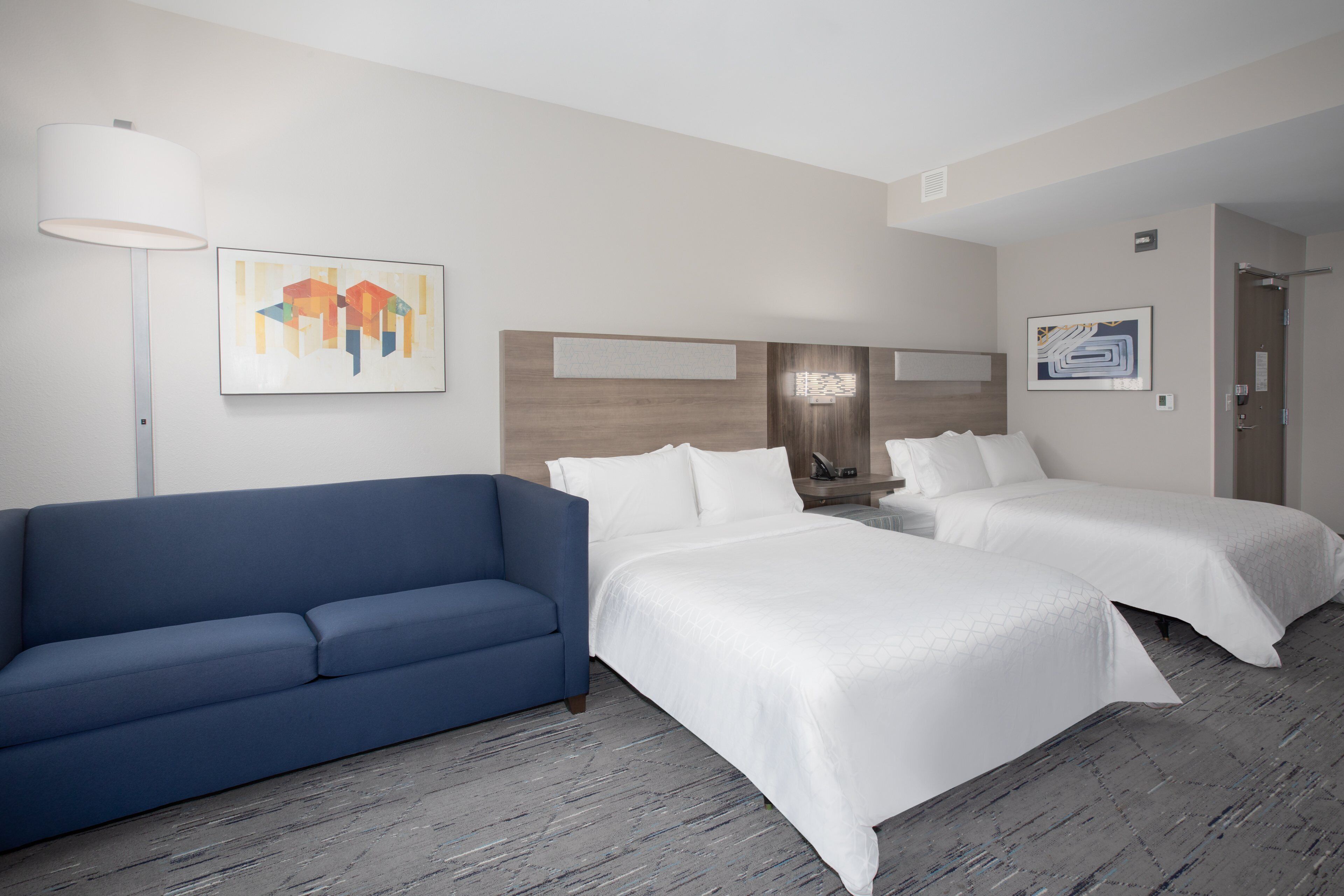 A hotel room with two beds, a blue sofa, and artwork on the walls.