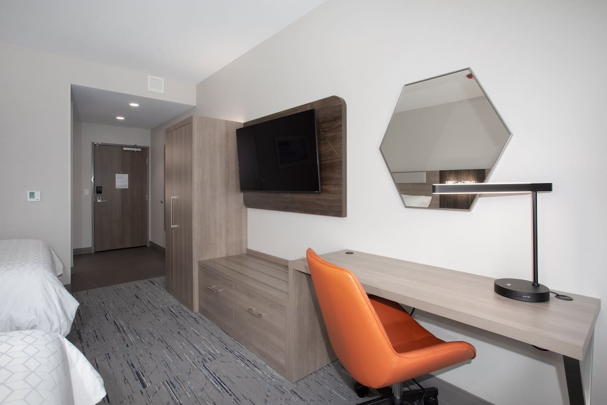 Moderni hotellihuone, jossa on sänky, työpöytä tuolilla, taulutelevisio ja suuri peili.