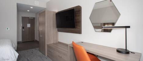 Une chambre d’hôtel moderne équipée d’un lit, d’un bureau avec une chaise, d’un téléviseur à écran plat et d’un grand miroir.