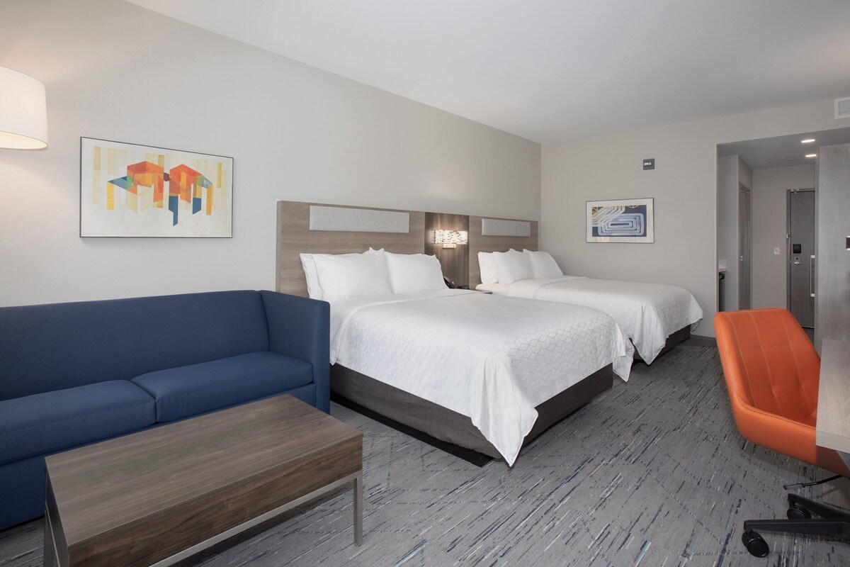 A hotel room with two beds, a blue sofa, an orange chair, and artwork on the walls.
