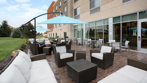 An outdoor patio area with wicker furniture, a blue umbrella, and a building with large windows in the background. - Holiday Inn Express and Suites Burley by IHG (Heyburn)