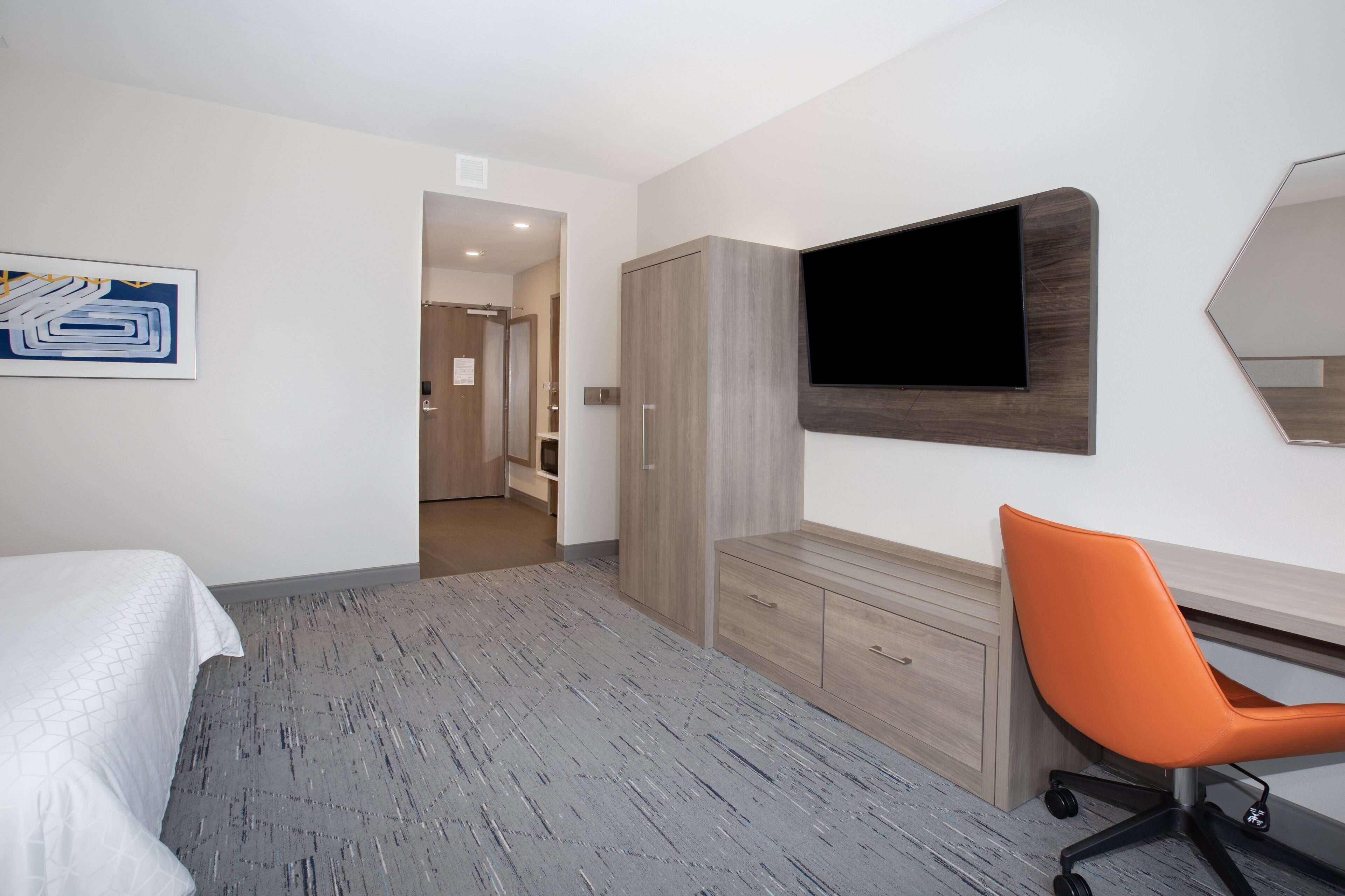 Ein Hotelzimmer mit Bett, Schreibtisch mit Stuhl, einem Wandfernseher und einem Kleiderschrank.