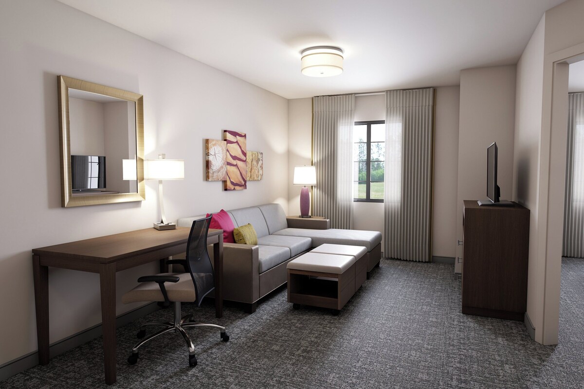 A hotel room with a desk, a sofa, a TV, and a cabinet.