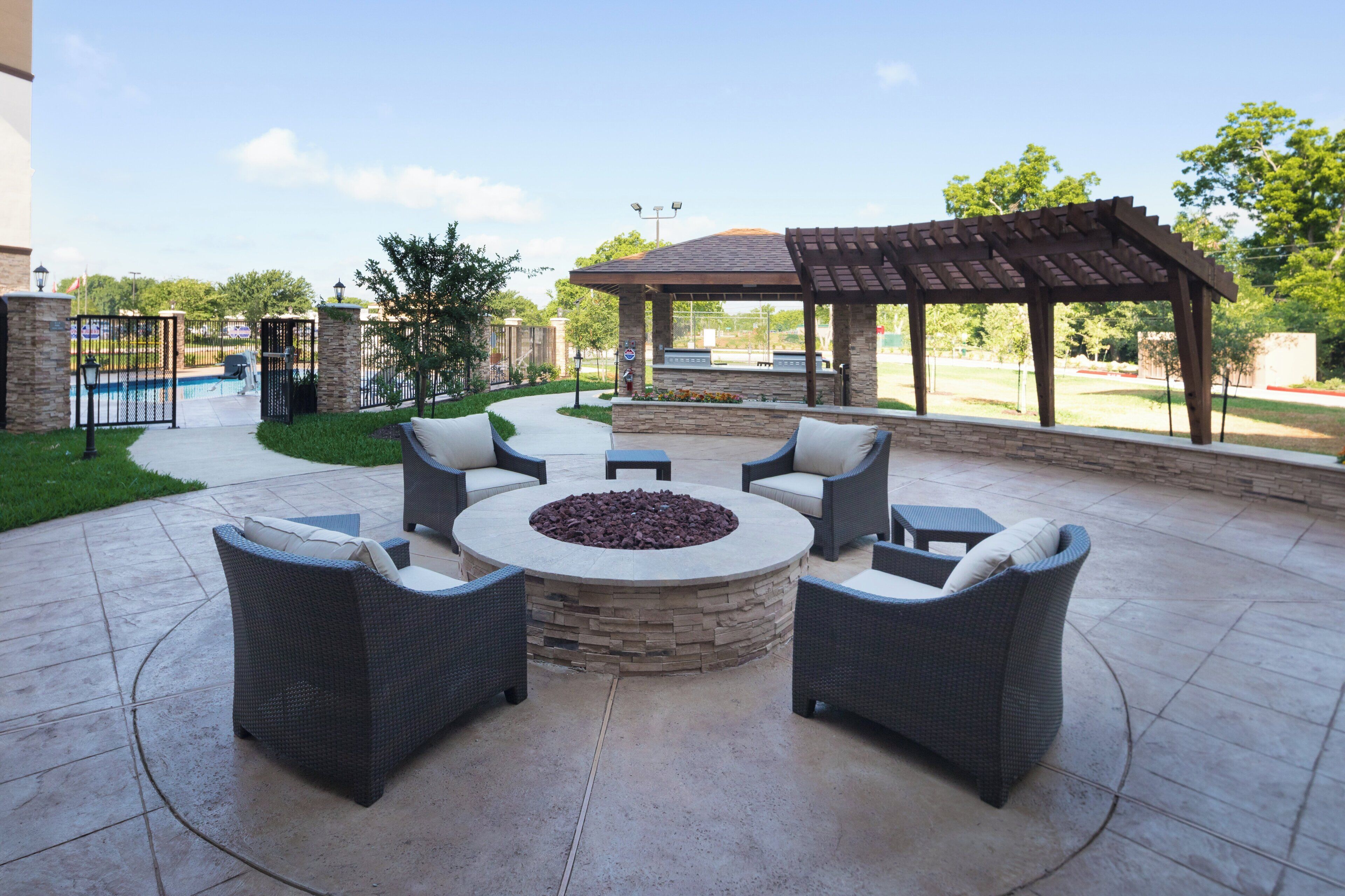 Un patio exterior con una zona de estar circular, un hogar para la chimenea y una pérgola.