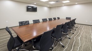 A conference room with a long wooden table, black chairs, a flat-screen TV on the wall, and patterned carpet flooring. - Staybridge Suites Southgate Detroit Area by IHG (Southgate)