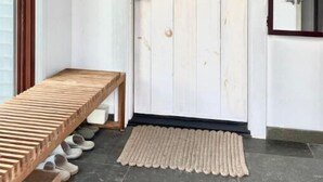 Uma porta branca com detalhe em madeira, um banco com sapatos e um tapete pequeno na entrada.