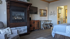 A cozy room with a stone fireplace, a television mounted on the wall, a small table with two chairs, and a bed with a patterned bedspread.