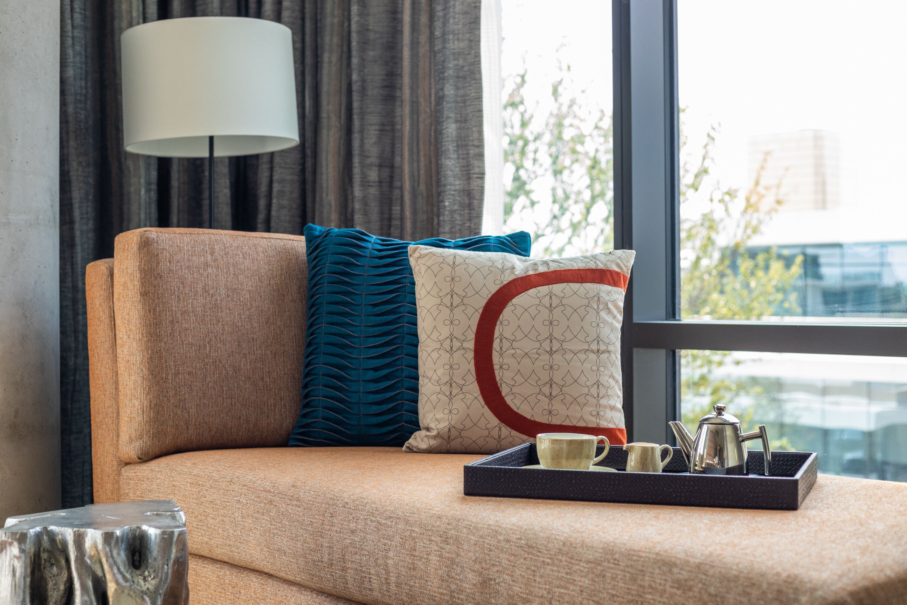 A sofa with a tray of tea set and a lamp in a room with a view of buildings.
