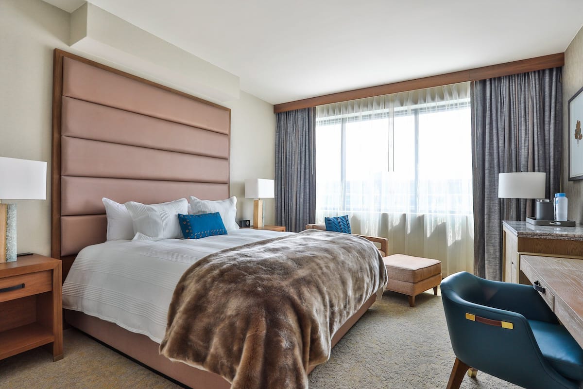 A hotel room with a large bed, a desk, a chair, and a window with curtains.
