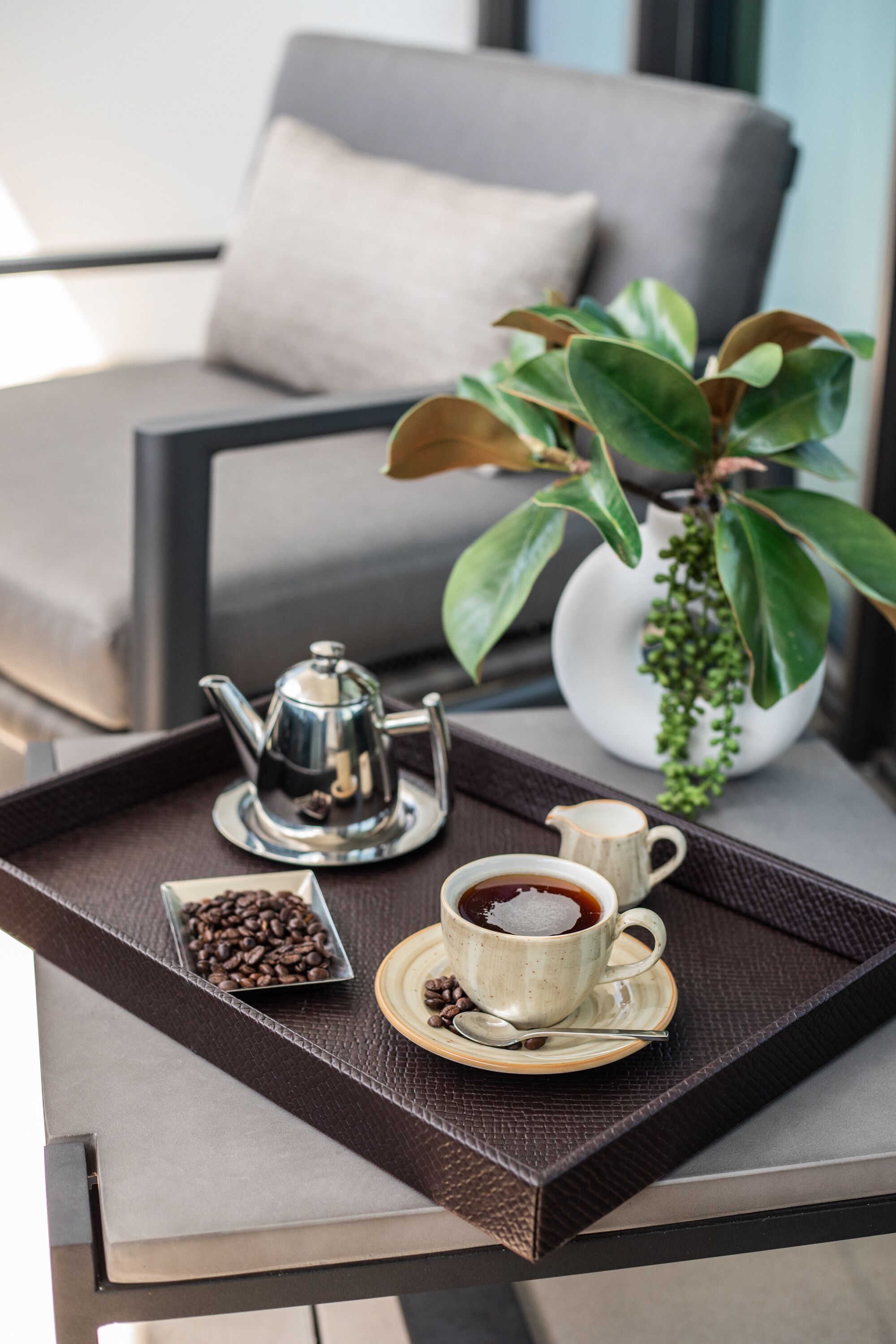 A tray with a coffee pot, cup, and saucer on a table, a bowl of coffee beans, and a potted plant.