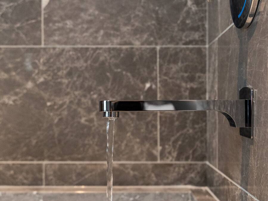 Een badkamer met een bad, een moderne kraan en marmeren tegels.