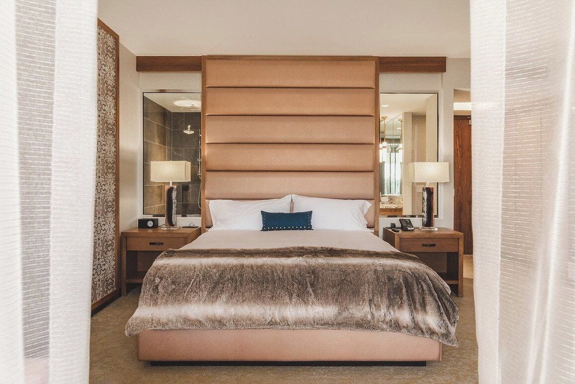 A hotel room with a large bed, two bedside tables with lamps, a mirror, and a patterned wall.