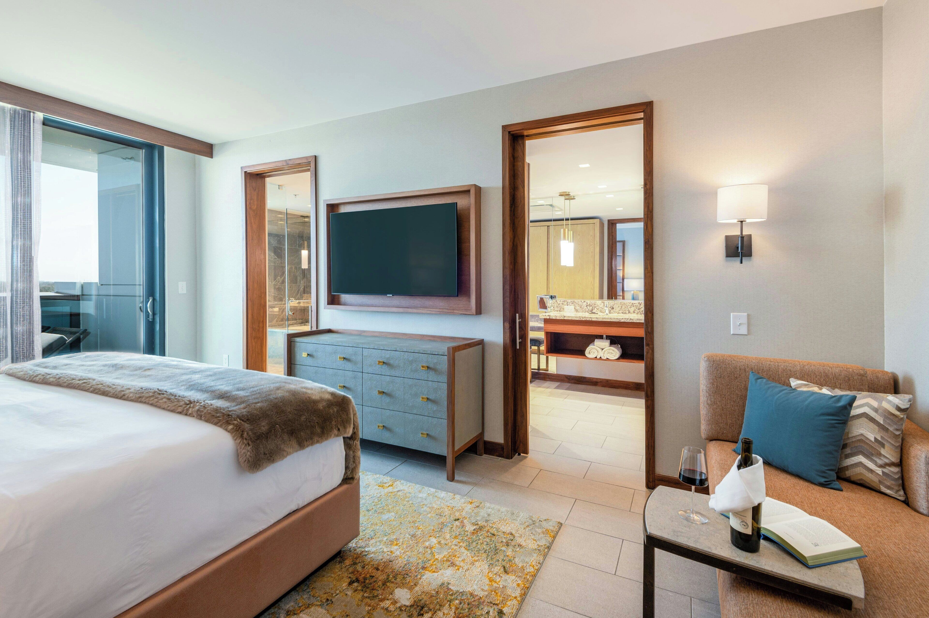 A hotel room with a bed, a TV, a dresser, a sofa, a coffee table, and a bathroom visible through an open door.