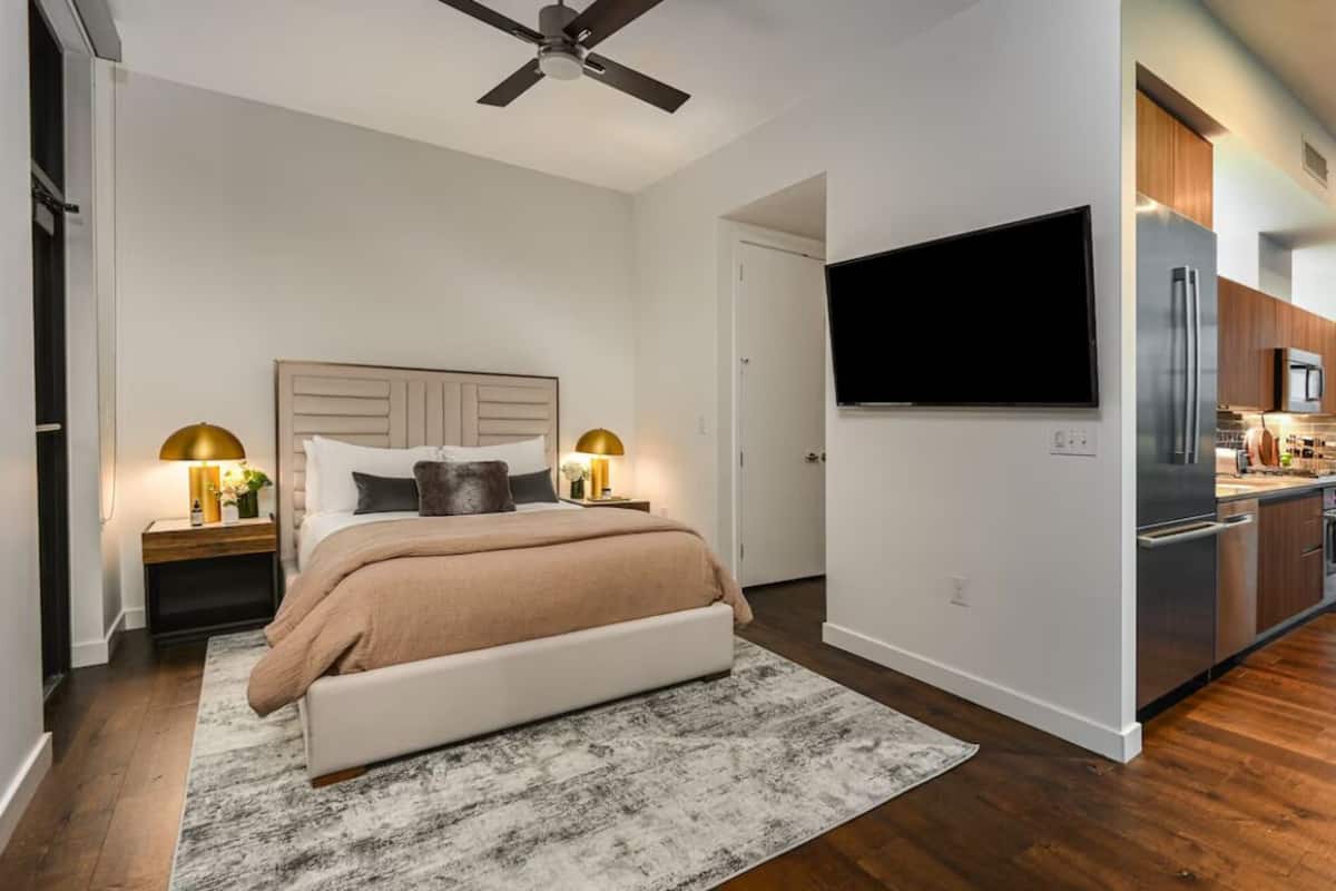 A modern bedroom with a bed, bedside lamps, a ceiling fan, and a TV mounted on the wall.