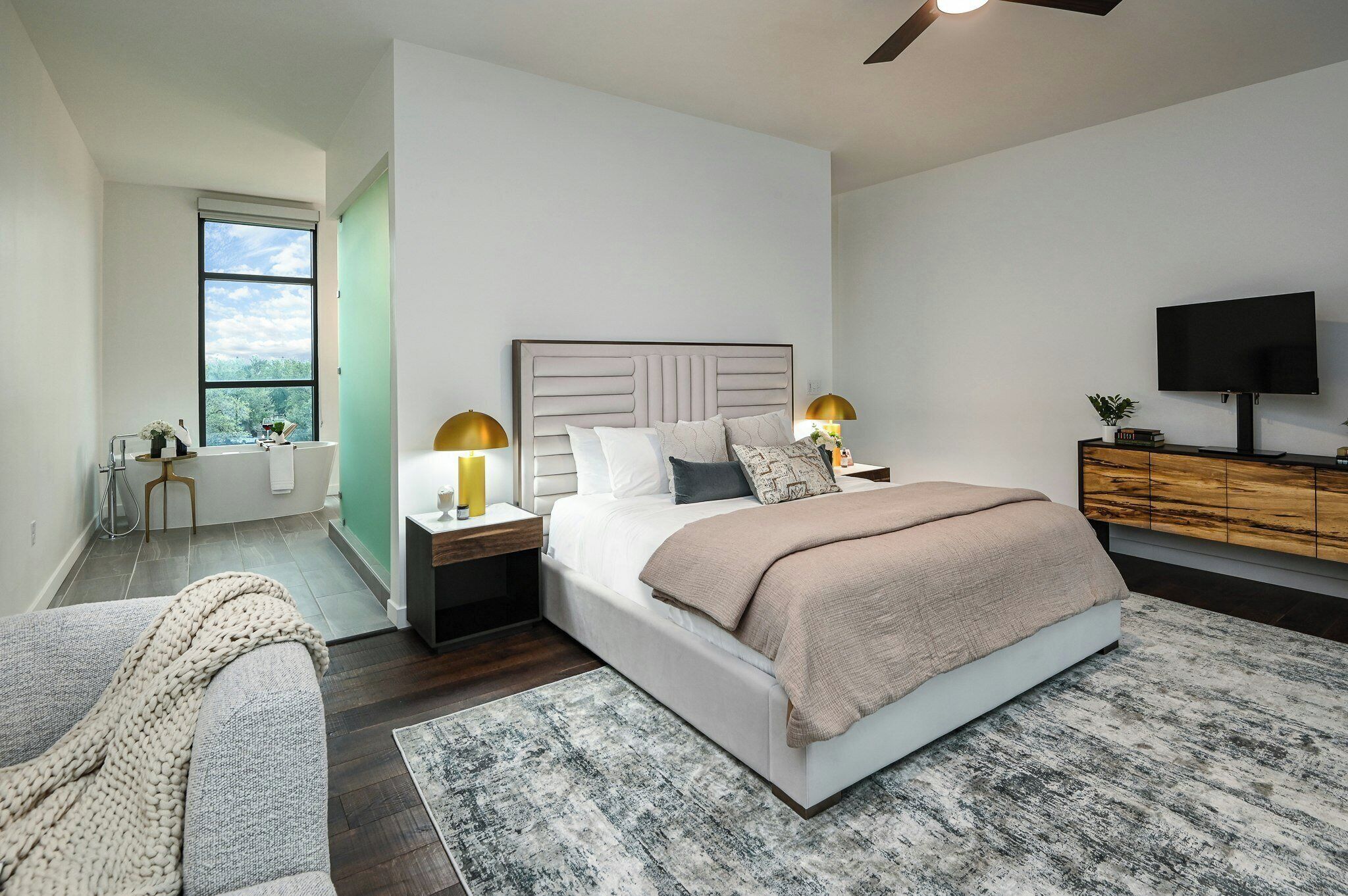 A modern bedroom with a large bed, bedside lamps, a TV, and a view of the outdoors.
