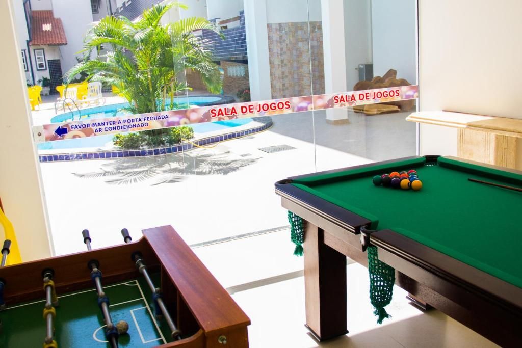 A pool table with a green felt surface and a foosball table in a room with a glass wall.