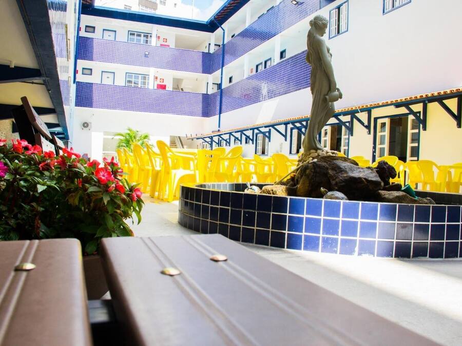 A hotel atrium with a central fountain, yellow chairs, and a statue.