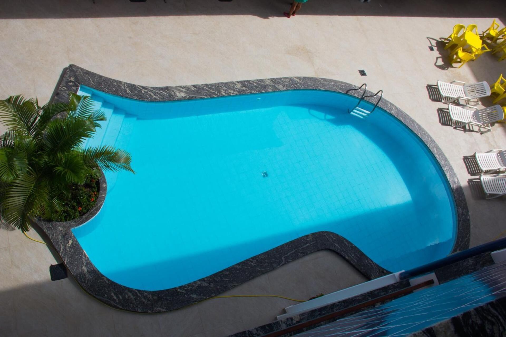 A swimming pool with a curved edge, surrounded by a tiled deck and a few lounge chairs.