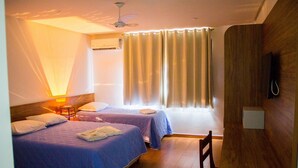 Une chambre d’hôtel avec deux lits, un ventilateur de plafond, un appareil de climatisation, une lampe de chevet, un téléviseur fixé au mur et une fenêtre avec des rideaux.