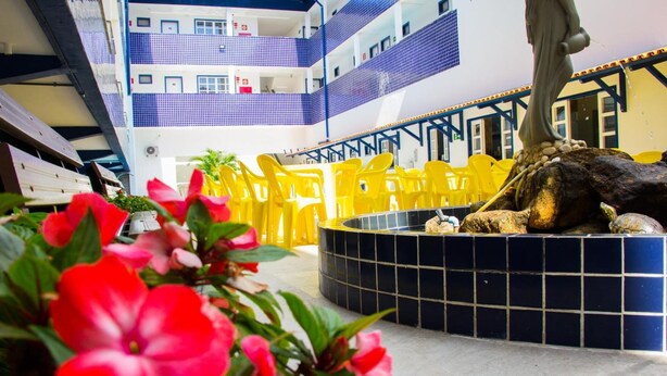 Un immeuble à plusieurs niveaux doté d’un atrium central où se trouve une fontaine circulaire ornée d’une sculpture de tortue, le tout entouré de chaises jaunes.