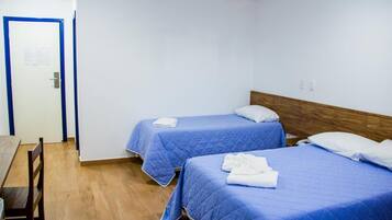 A room with two beds, each with a blue bedspread and white pillows, a wooden headboard, and a wooden table with chairs.