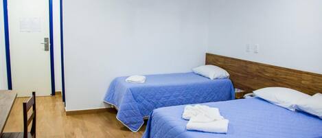 A room with two beds, each with a blue bedspread and white pillows, a wooden headboard, and a wooden table with chairs.