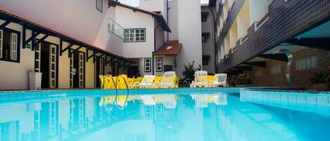 Una piscina con sillas amarillas, un área de descanso techada y un edificio con varios balcones.
